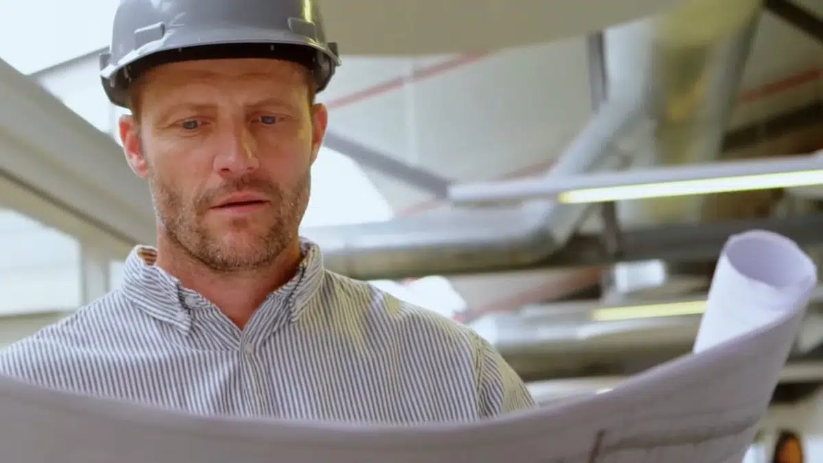 Licensed plumber reviewing plans below exposed piping for Plumbing Services in Bellflower, CA